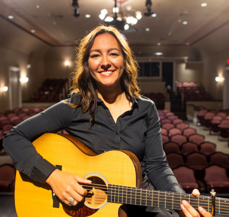 A woman performing on stage with her guitar. A woman sitting on a stage and holding a guitar.